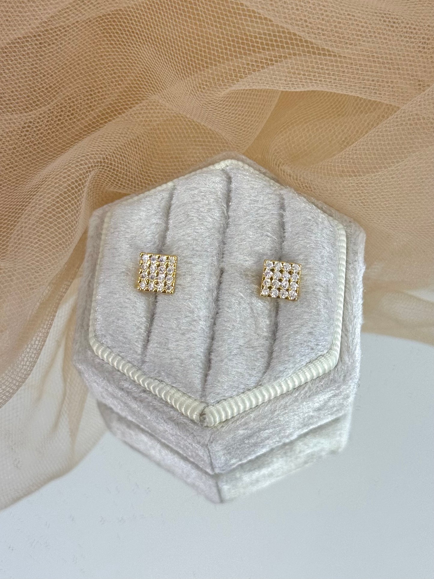 Gold square earrings on a gray hexagonal jewelry display with a beige fabric background, dangling, dainty, everyday wear