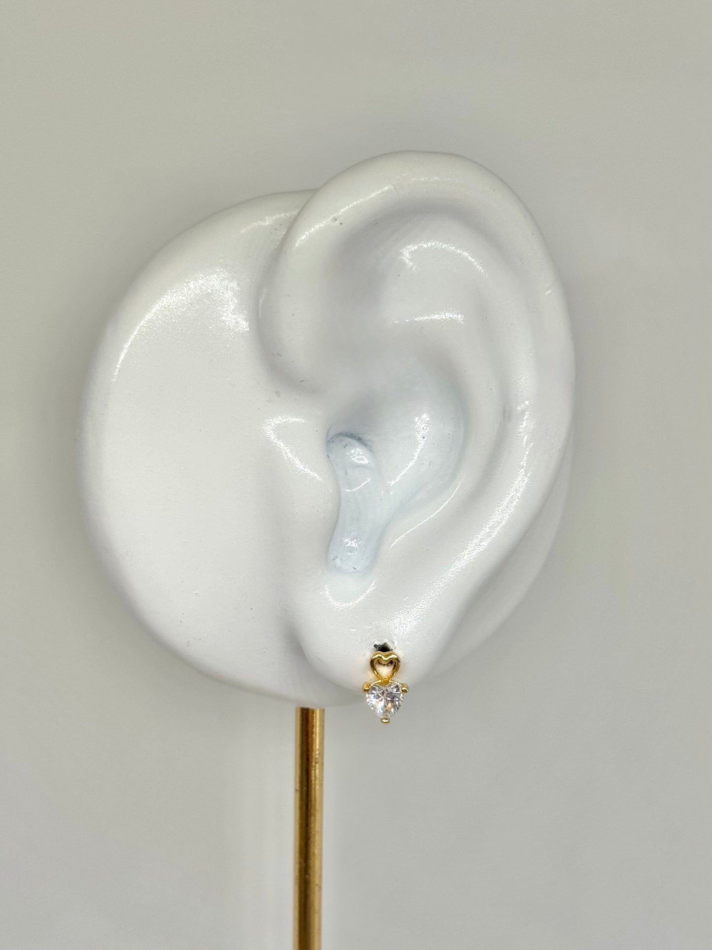Earring displayed on a white ear model against a gray background, heart shaped, heart stud earrings, stud earrings, minimalist yellow gold, everyday wear