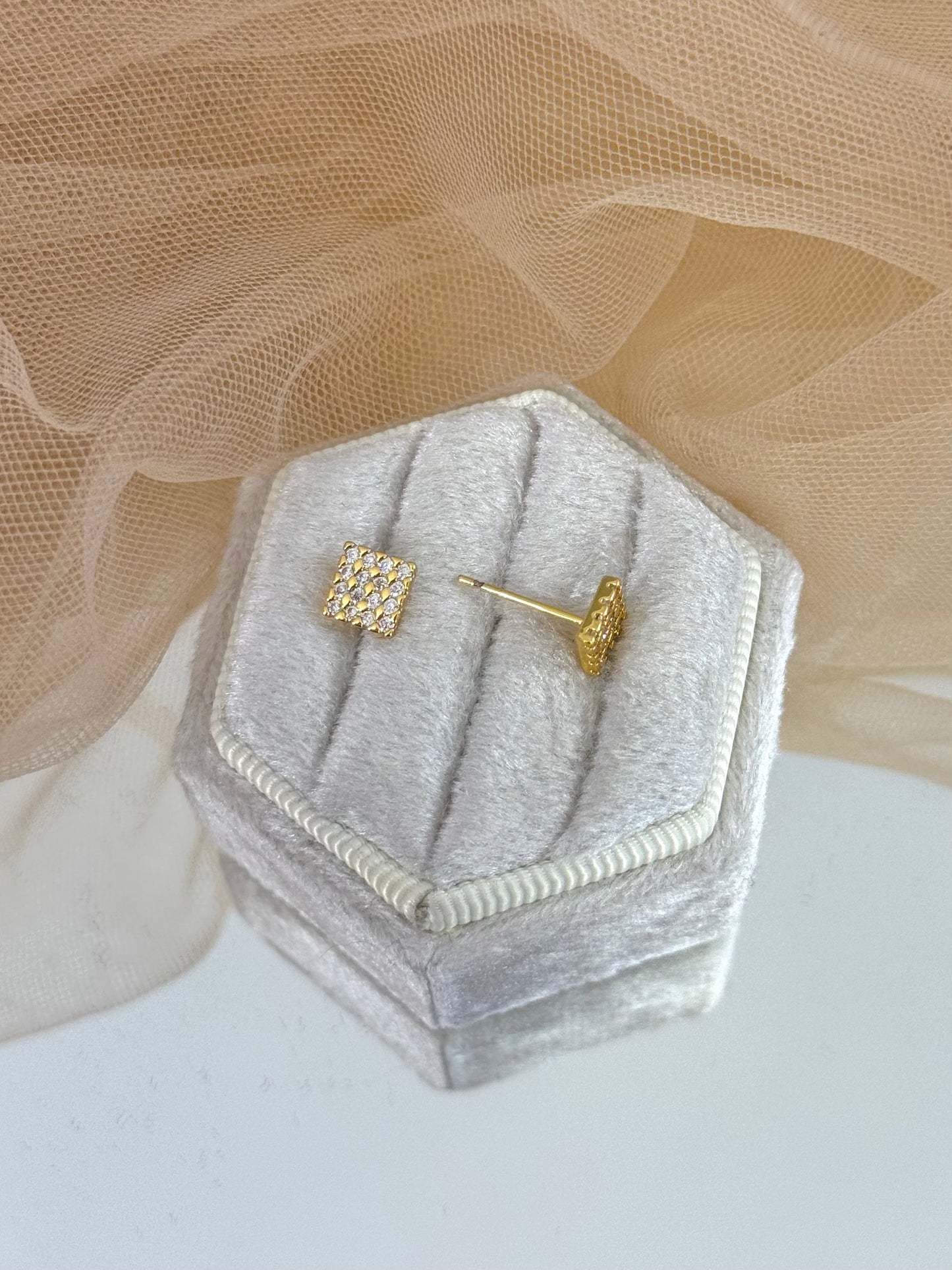 Gold square earrings on a gray hexagonal jewelry display with a beige fabric background, dangling, dainty, everyday wear