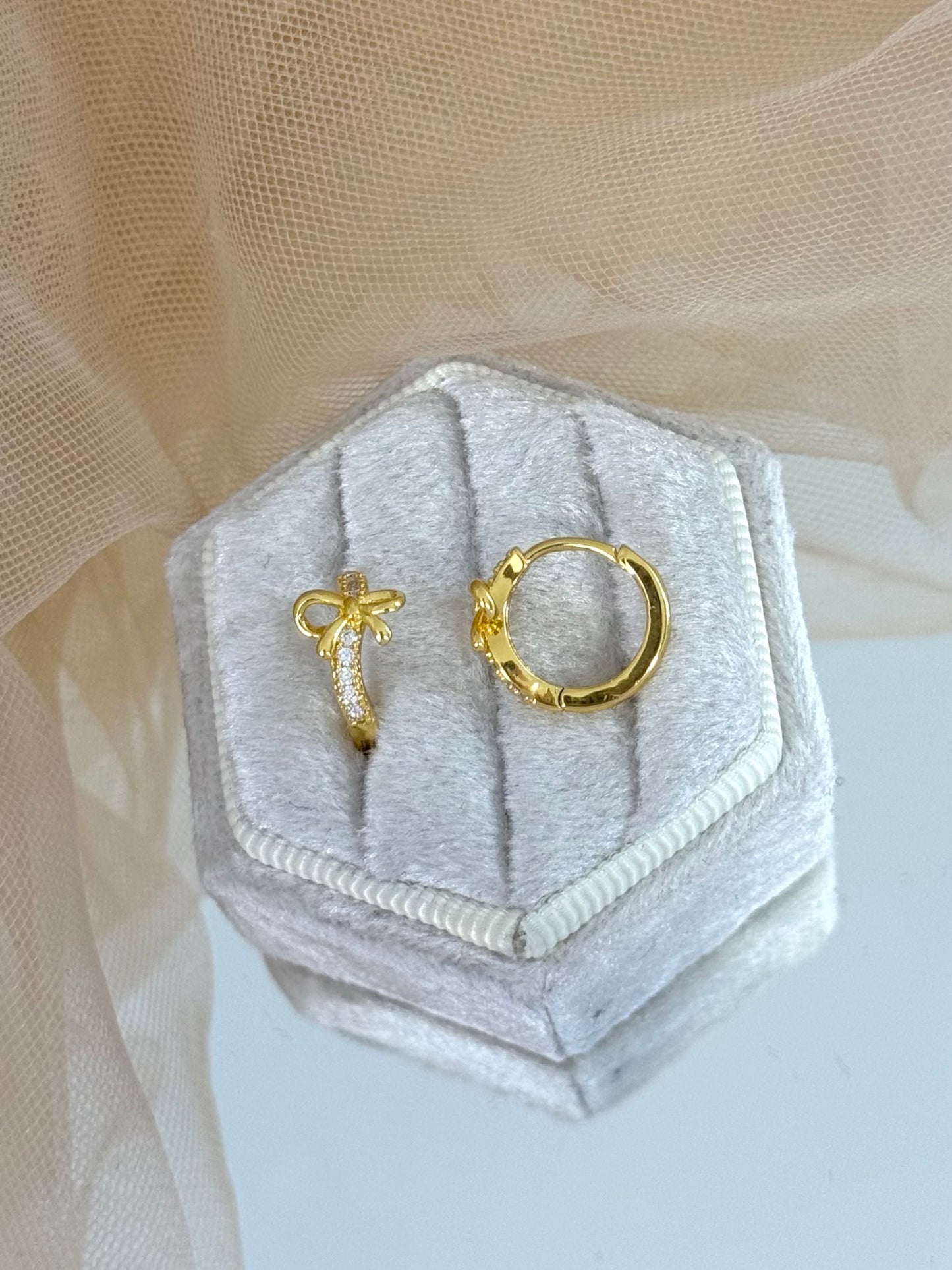Gold bow-shaped earrings in a hexagonal gray velvet box on a beige fabric background, bow, bow earrings, bow stud earrings, perfect gift for her, modern design earrings, minimalist look, classic look, elegance, everyday wear