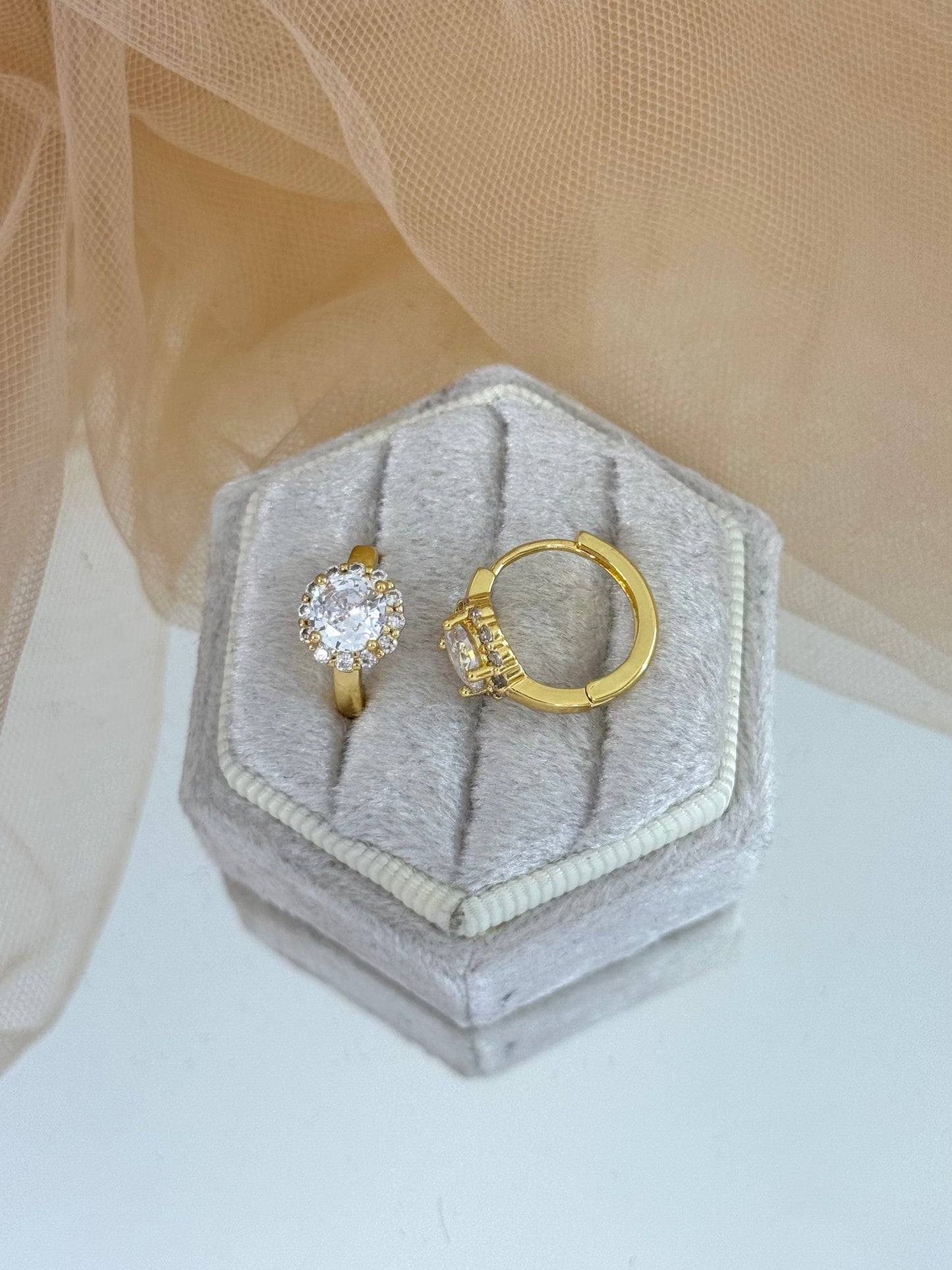 Gold earring with a diamond on a hexagonal gray velvet box against a beige fabric background, gemstone, faceted gemstone, everyday wear, stud earrings
