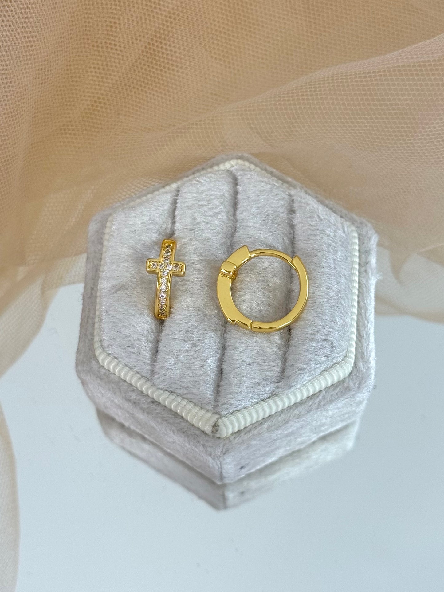Gold cross and hoop earrings on a hexagonal gray jewelry box with a beige background, stud cross earrings, everyday wear, minimalist look, shiny yellow gold, modern earrings