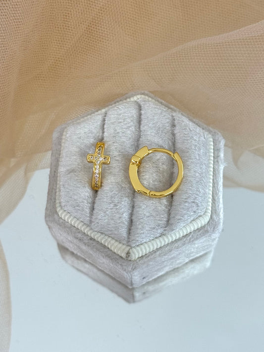 Gold cross and hoop earrings on a hexagonal gray jewelry box with a beige background, stud cross earrings, everyday wear, minimalist look, shiny yellow gold, modern earrings