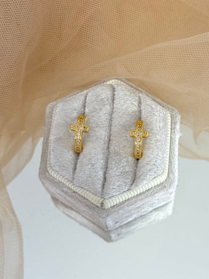 Gold cross and hoop earrings on a hexagonal gray jewelry box with a beige background, stud cross earrings, everyday wear, minimalist look, shiny yellow gold, modern earrings