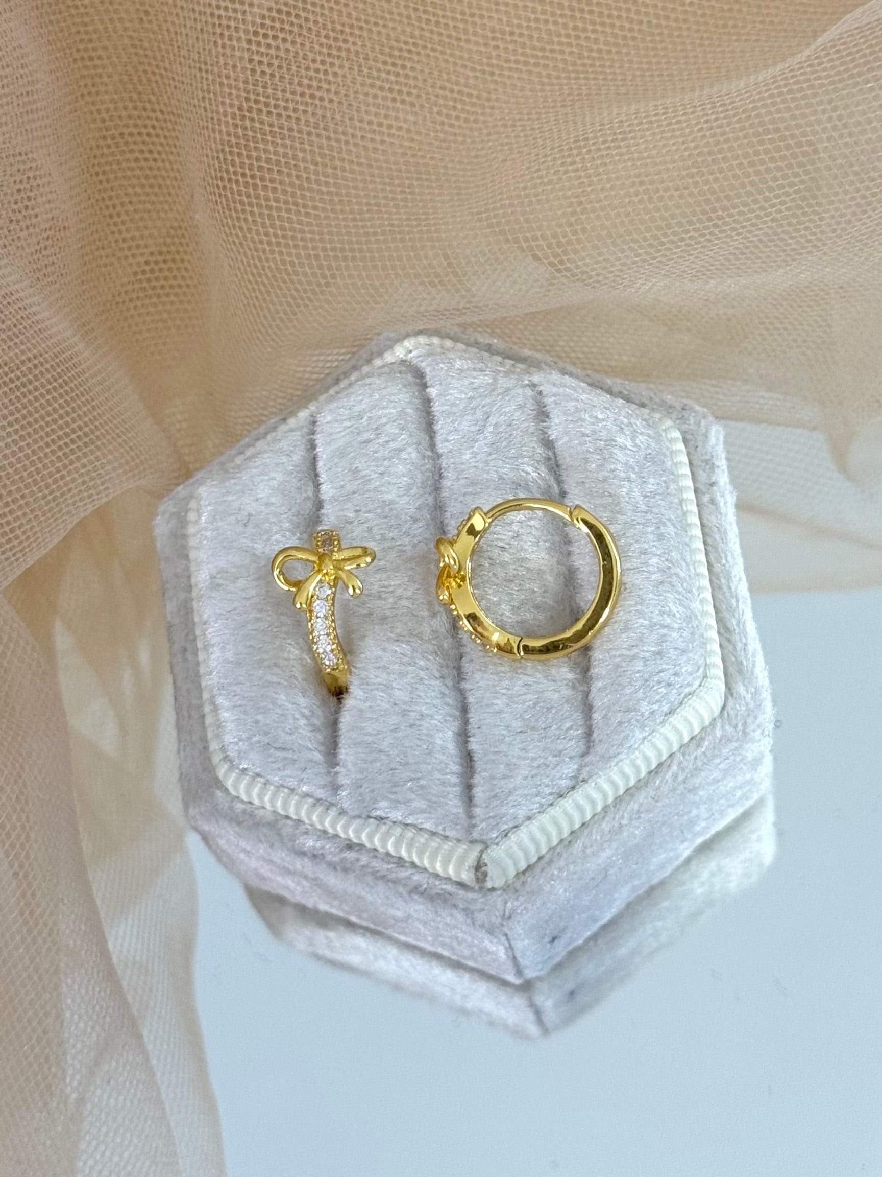 Gold bow-shaped earrings in a hexagonal gray velvet box on a beige fabric background, bow, bow earrings, bow stud earrings, perfect gift for her, modern design earrings, minimalist look, classic look, elegance, everyday wear